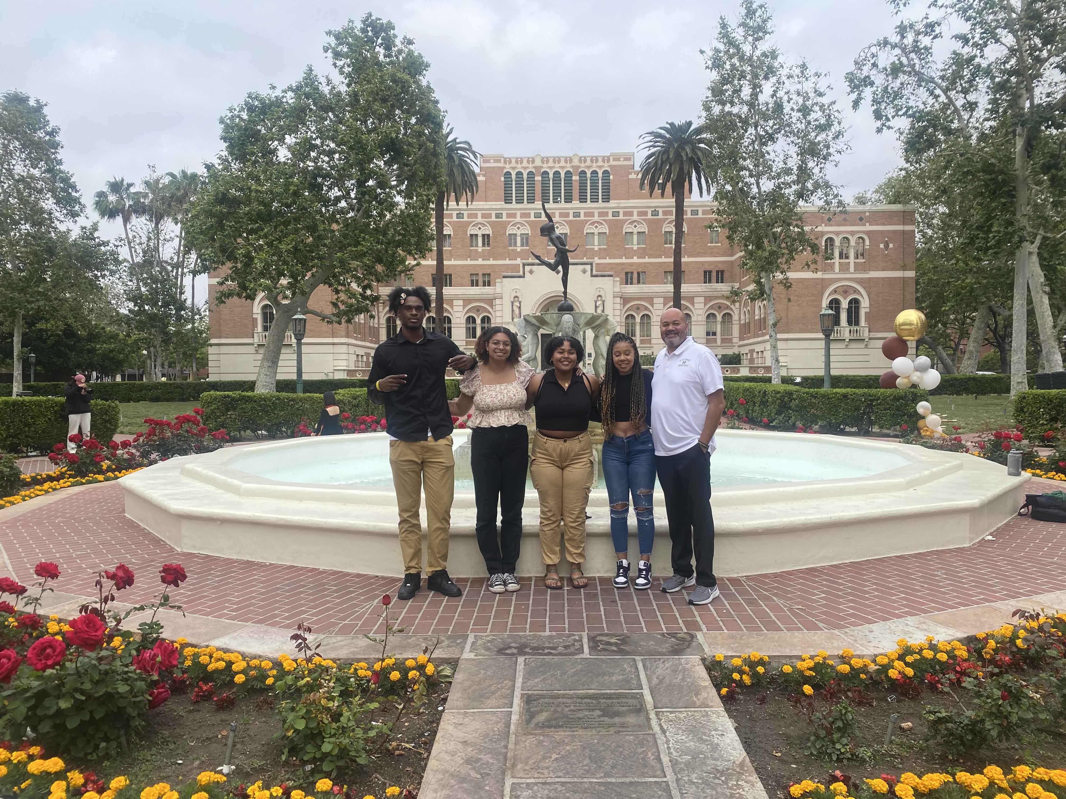 Black student athletes and advisor pose for a photo in front of a fountain. 